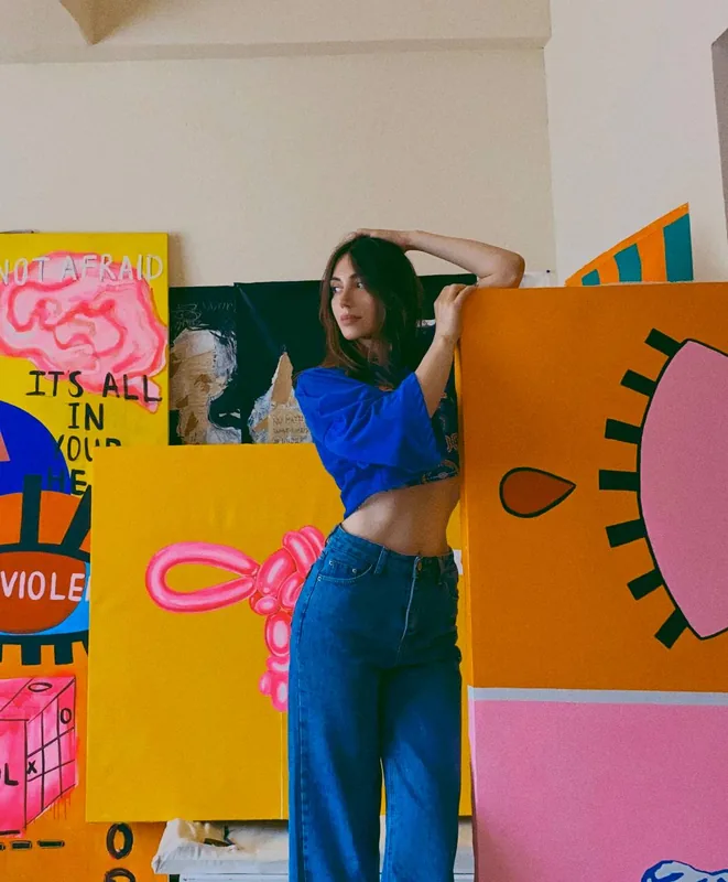 Lusin Ginosyan in her studio, leaning on a large orange canvas, surrounded by her paintings